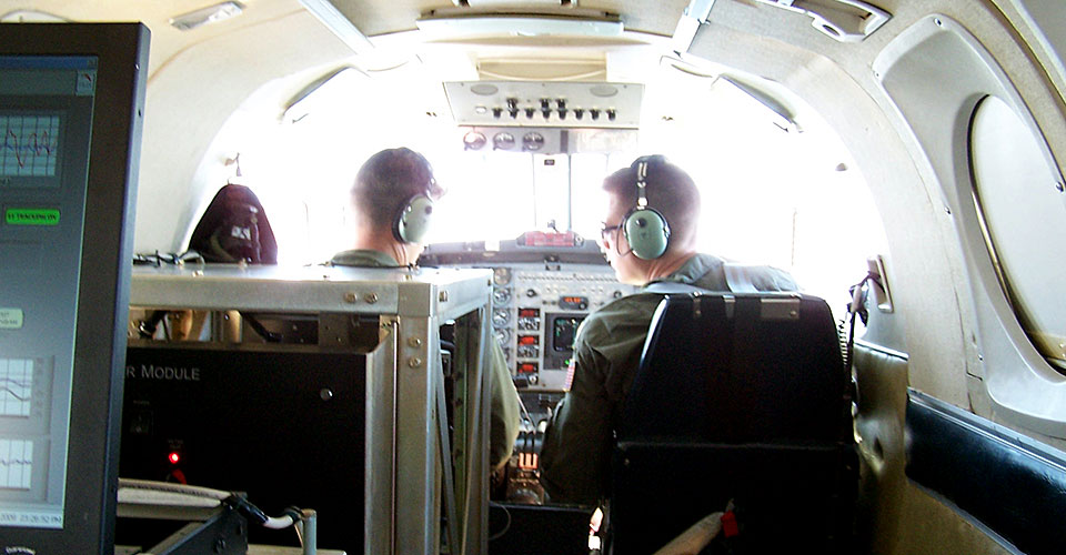 The pilot and co-pilot of a Navy-owned King Air aircraft prepare for takeoff on a data collection flight with GRAV-D instruments (fore and mid-ground) and a GRAV-D operator as their payload.